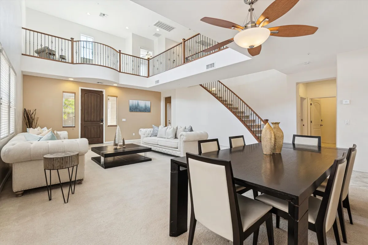 This image captures a spacious open-plan living and dining area, featuring a large sectional sofa arranged for group gatherings, a prominent dining table set for meals, a stylish staircase, and decorative vases. The scene exudes an inviting and comfortable mood, ideal for family gatherings, celebrations, and quiet evenings.