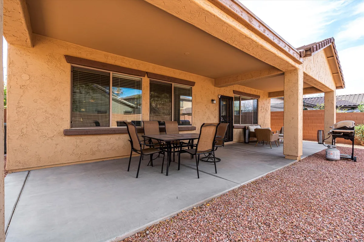 A welcoming backyard scene featuring a dining table with comfortable chairs and a grill set up on a patio. The fenced yard provides a sense of privacy and security, perfect for families to gather and kids to play safely. The Arizona sky is visible above, hinting at the possibility of al fresco meals and relaxed evenings outdoors.