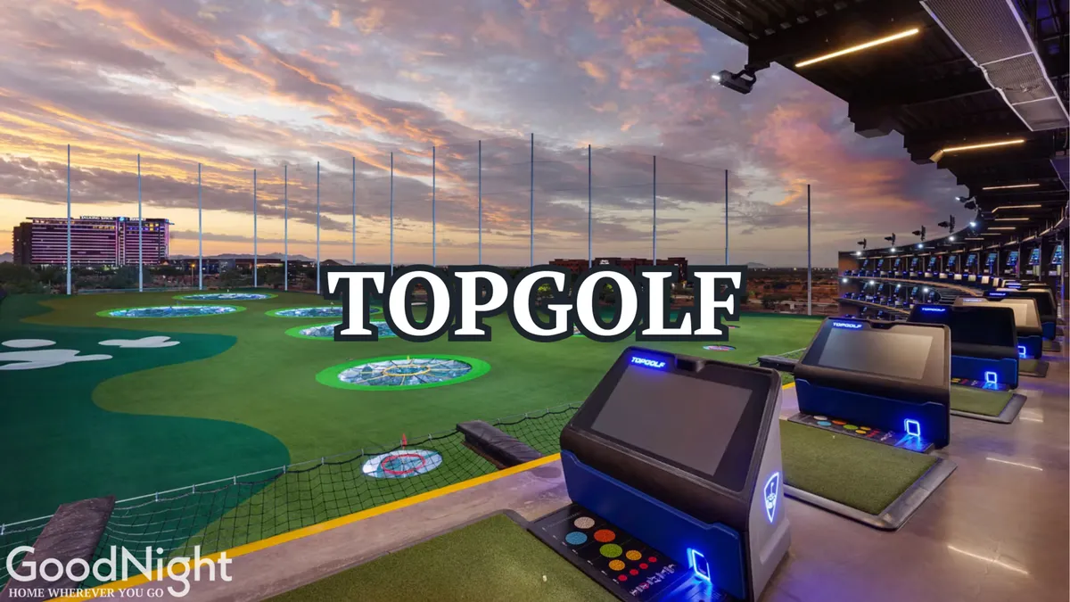 Golf hitting bays with colorful target greens are set beneath a dusk sky, with people enjoying the social, energetic atmosphere as they play, eat, and take photos.